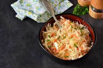 Marinated sour cabbage with onions and spices on black backgroun