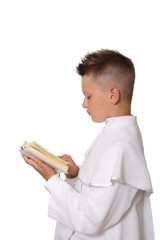 Pierwsza komunia święta, chłopiec w białej albie czyta książeczkę.
