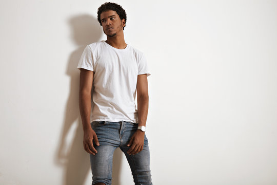 Thoughtful black young man in blank white t-shirt and jeans isolated on white background and looks aside