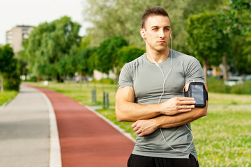 Outdoor runner man tuning his music player during jogging.