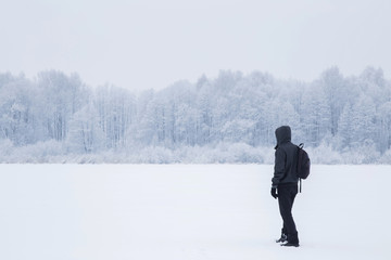 Young man walking and breathing fresh air in a white snowy countryside forest. Tree branches are snow covered. Winter day.