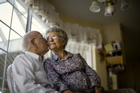 Affectionate elderly couple sit at the kitchen window together.