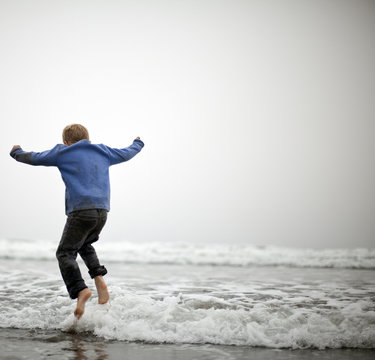 Small boy jumping in shallow water at beach.