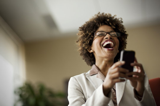 Businesswoman laughing as she looks at cell phone.