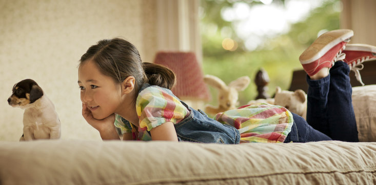 Young girl daydreaming while lying on her bed next to a puppy.