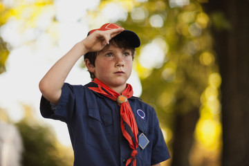 Boy Scout salutes while standing on a suburban street.