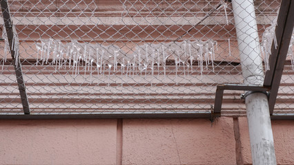 A lot of icicles on a metal safety grid of the facade of building.