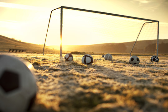 Soccer balls on an empty field at sunset
