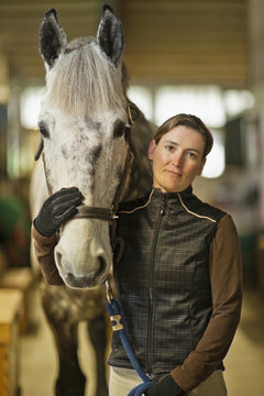 Portrait of a mid adult woman and her horse in a stable.
