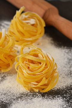 Raw tagliatelle pasta with flour on a black background