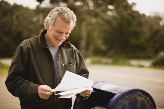 Man standing next to post box reading letter