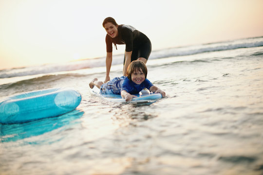 Mother teaching young son how to ride a wave on a surfboard.