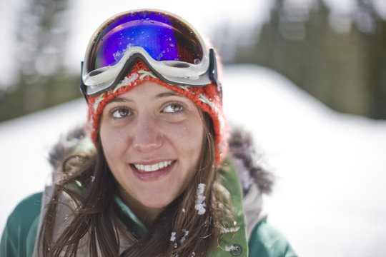 Smiling young woman wearing ski goggles  on her forehead.