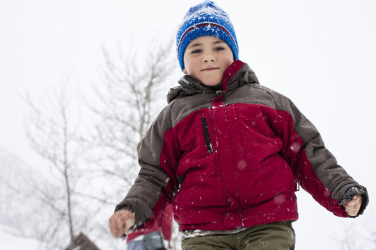 Portrait of a young boy wearing a padded jacket and knit hat while playing in the snow.