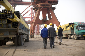 Group of business people wearing hard hats walking along a wharf.