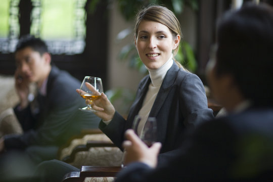 Young businesswoman holding a glass of alcohol while seated with colleagues in a restaurant.