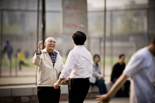 Two mature men playing basketball in a park.