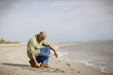 Mature adult man drawing in the sand on a beach.