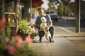 Mid-adult man crouching with a small dog on the street.