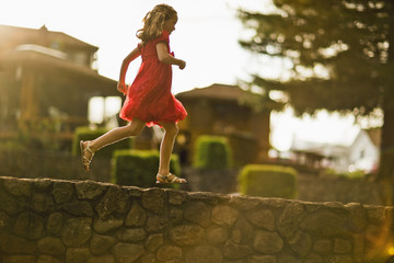 Young girl running along a stone wall.