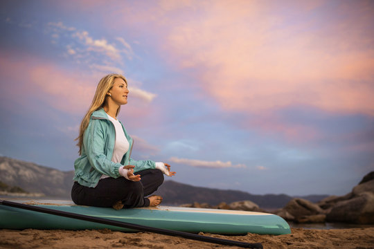 Young woman meditating on her paddleboard.