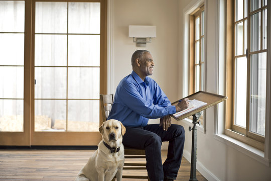 Smiling man sits at desk with dog and looks out of the window