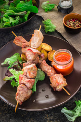 Shish kebab with greens, potatoes and sauce on ceramic plate