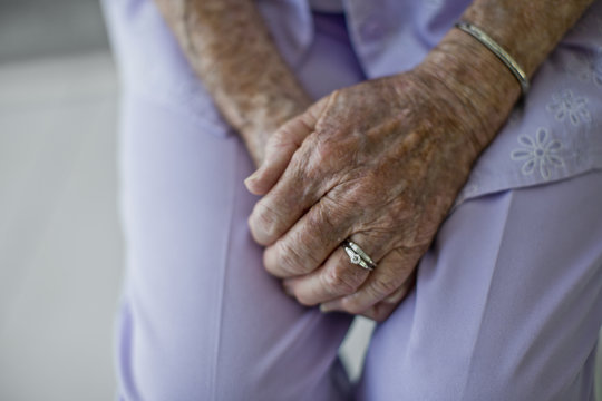 Hands of an elderly woman clasped in her lap.