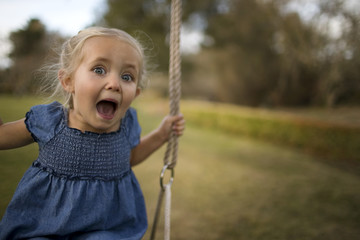 Portrait of a little girl playing on swing in the garden