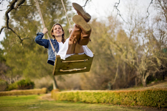 Happy young woman swinging on a wooden rope swing.