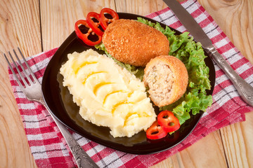 two fried breaded cutlet with mashed potatoes and lettuce on a black plate wooden background