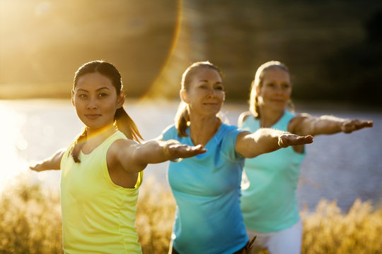 Three women practicing yoga in a rural field.