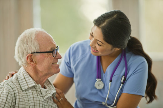 Smiling female nurse comforting an elderly male patient.