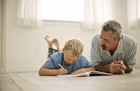 Father helping his son with homework while lying on floor