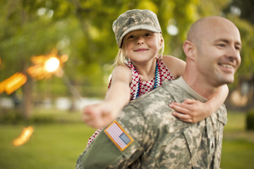 Smiling male soldier piggy-backing his young daughter in their back yard.
