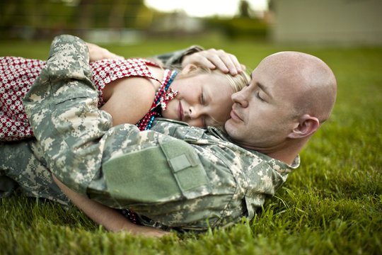 Male soldier hugging his young daughter while lying on the grass in their back yard.