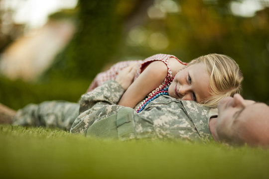 Male soldier and his young daughter while lying on the grass in their back yard.