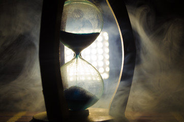 Time concept. Silhouette of Hourglass clock and smoke on dark background with hot yellow orange red blue cold back lighting, or symbols of time with copy space, sandglass or sand clock