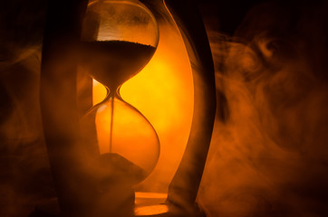 Time concept. Silhouette of Hourglass clock and smoke on dark background with hot yellow orange red blue cold back lighting, or symbols of time with copy space, sandglass or sand clock