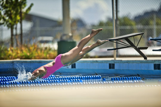 Woman dives from a diving platform into a swimming pool.