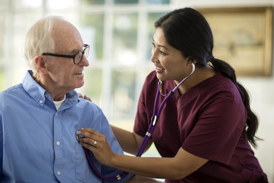 Smiling senior man having a conversation with a female nurse as she listens to his heartbeat through a stethoscope.