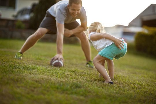 Mid adult man playing American football with his daughter on a lawn.