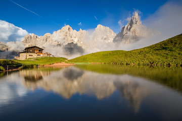 The Pale di San Martino peaks (Italian Dolomites) reflected in the water, with an alpine chalet on...