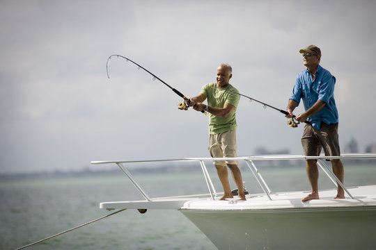 Two smiling mature men fishing off the edge of a boat together in the ocean.