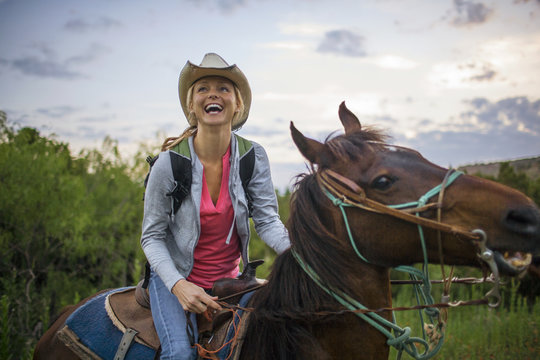 Happy young woman laughs with joy as she has fun horse riding in a rugged nature reserve.