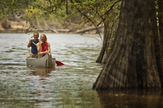 Smiling mature couple canoeing on a river in the woods.
