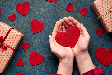 Heart Symbol of love in female hands. The concept of declarations of love. Valentines day background with hearts and a gift boxes on concrete board. Flat lay. Top view.