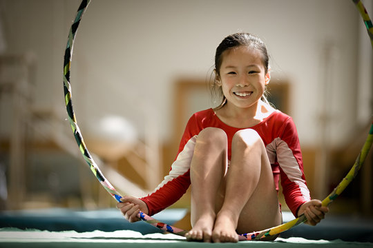 Portrait of a girl playing around with a hula hoop in a gym.