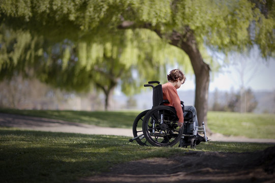 Young boy wheeling himself in a wheelchair at the park.