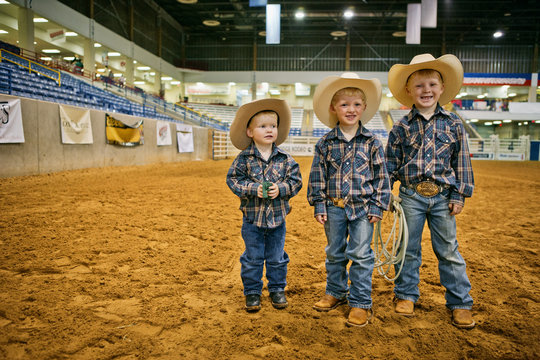 Portrait of three smiling young boys dressed as cowboys at a rodeo arena.